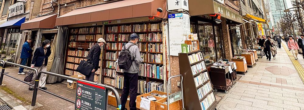Libreria con libri antichi a Jimbocho, Tokyo, con persone sul marciapiede.
