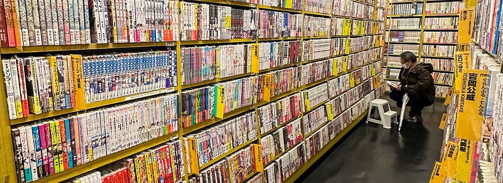 Scaffali pieni di manga in un corridoio di Mandarake con una persona che legge.