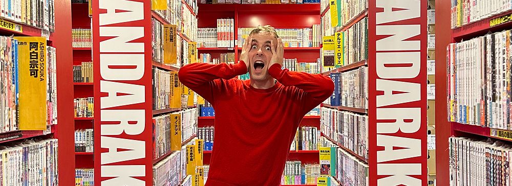 Persona in maglia rossa tra scaffali di manga a Mandarake.