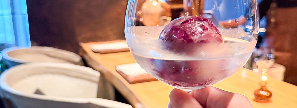 Un calice con cocktail e una sfera di ghiaccio tenuto in mano all'interno del bar Memento Mori a Tokyo.