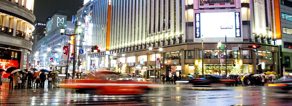 Mitsukoshi Ginza a Tokyo di notte sotto la pioggia con taxi e persone.