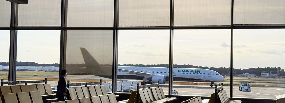 Veduta interna di una sala d'attesa all'aeroporto di Narita con un aereo Eva Air visibile attraverso una grande vetrata.