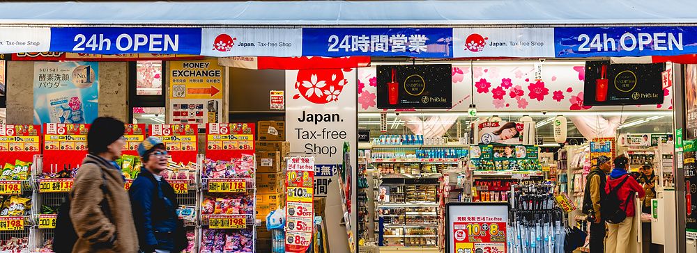 Facciata di un negozio Tax-free a Osaka con insegne luminose e persone che camminano sul marciapiede antistante.