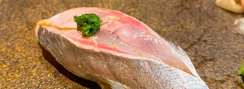 Un nigiri di aji con guarnizione verde servito su un piatto in ceramica scura da Sushi Takeuchi a Tokyo.