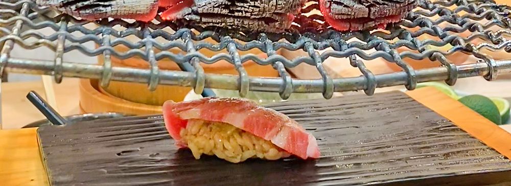Un nigiri di otoro scaldato coi carboni ardenti da Sushi Tou con uno chef che maneggia la brace su una griglia.