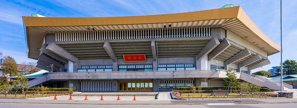 Facciata esterna del Nippon Budokan a Tokyo con tetto dorato sotto un cielo limpido e azzurro.