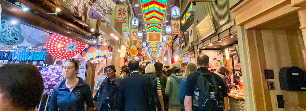 Persone camminano nel mercato coperto del Nishiki Market di Kyoto, con luci colorate sul soffitto.