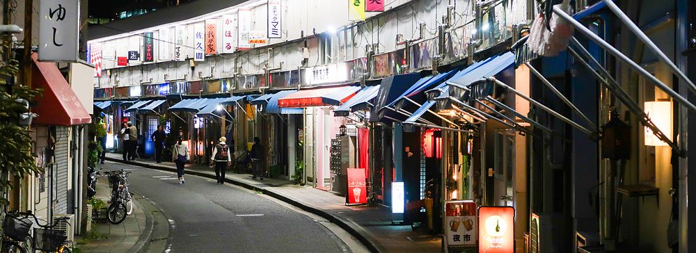 Strada curva a Noge, Yokohama, di notte con negozi e insegne luminose.