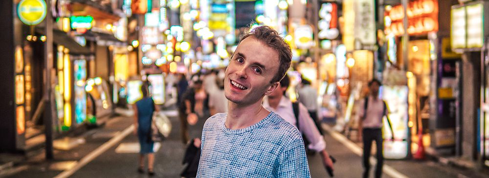 Marco Togni sorridente su strada affollata con insegne al neon a shinjuku.
