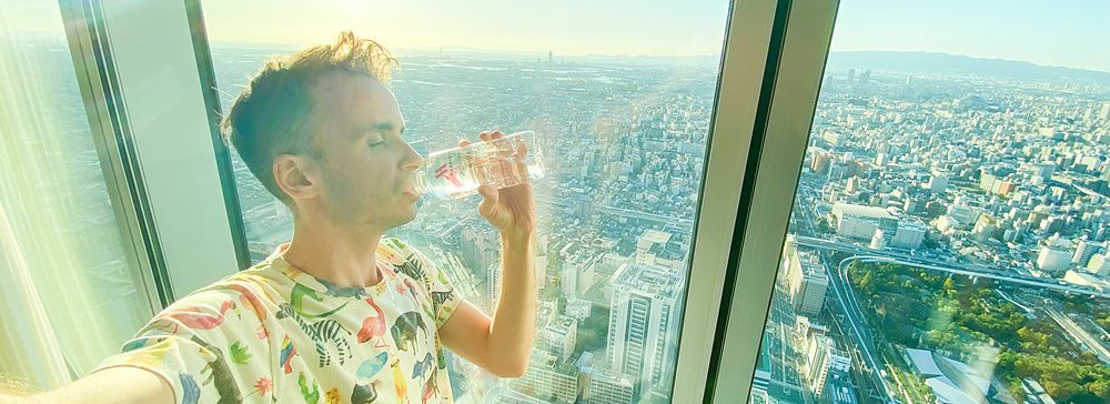 Una persona beve accanto a una finestra in una stanza d'hotel con vista sulla città.