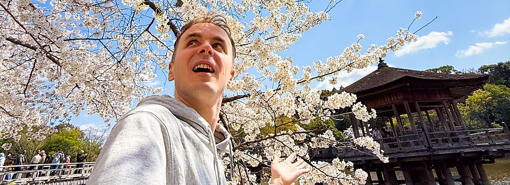 Selfie di Marco Togni al parco di Nara, in primavera, con i fiori di ciliegio e il padiglione Ukimido sullo sfondo.