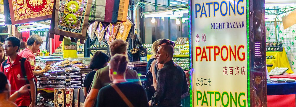 Scena notturna vivace al Patpong Night Bazaar di Bangkok con insegne luminose e bancarelle.