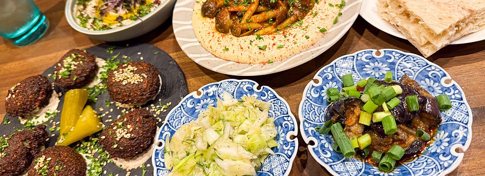 Piatti di falafel, hummus con funghi e pane pita serviti su un tavolo in legno nel ristorante Telaviv a Kyoto.