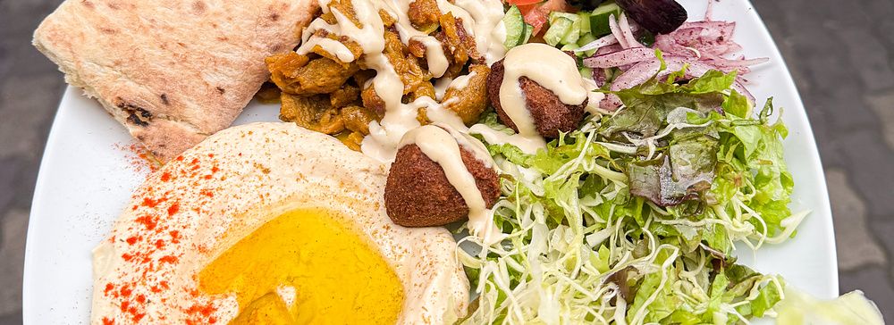 Un piatto misto vegano a Falafel Sababa composto da hummus, falafel, insalata e pane pita tenuto in mano a Namba, Osaka.