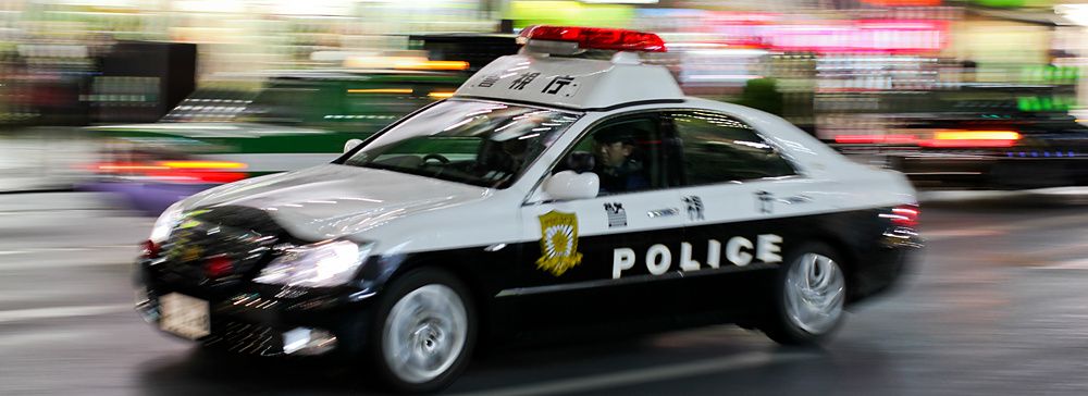 Volante della polizia giapponese in transito notturno lungo una strada urbana in Giappone.