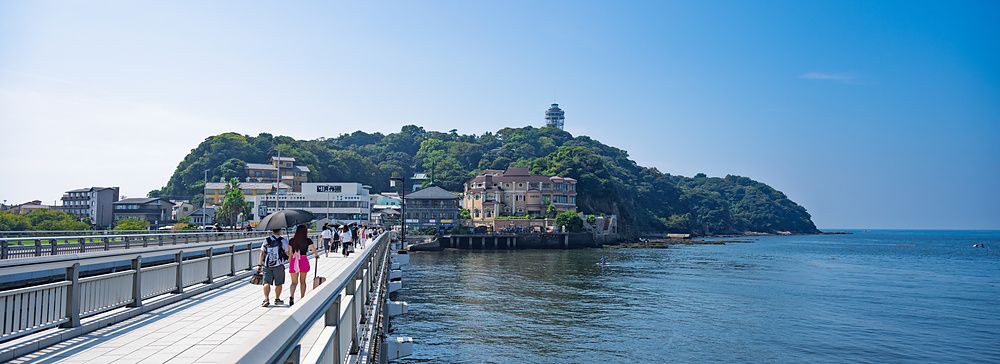 Persone che percorrono il ponte Enoshima Benten verso l'isola di Enoshima in una giornata di sole.