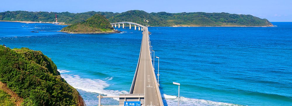 Ponte di Tsunoshima che attraversa il mare blu verso un'isola verde sotto un cielo sereno.