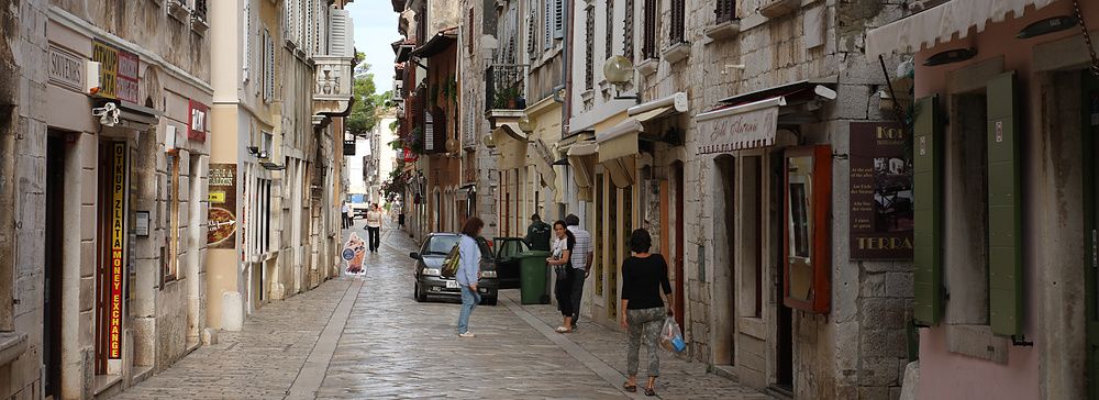 Strada del centro storico con negozi a Porec, Croazia, persone passeggiano.