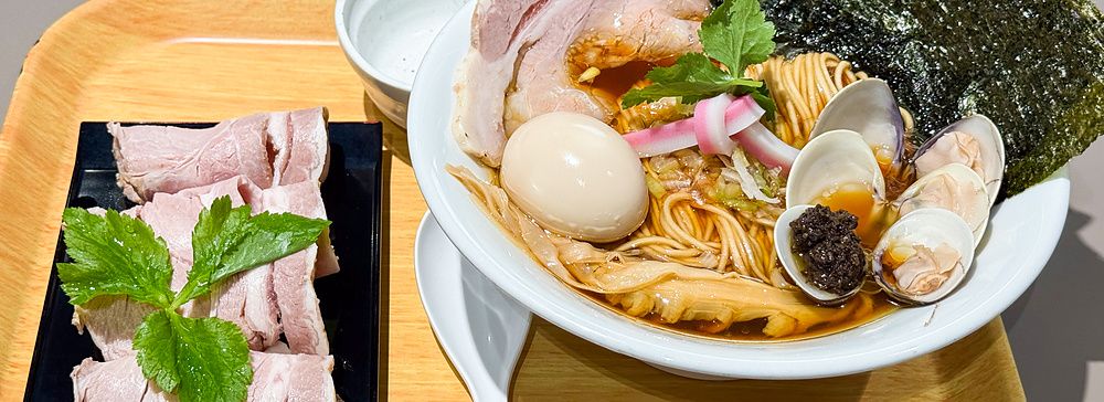 Una ciotola di ramen con vongole e carne servita su un vassoio di legno presso il ristorante Mugi to Olive a Tokyo.