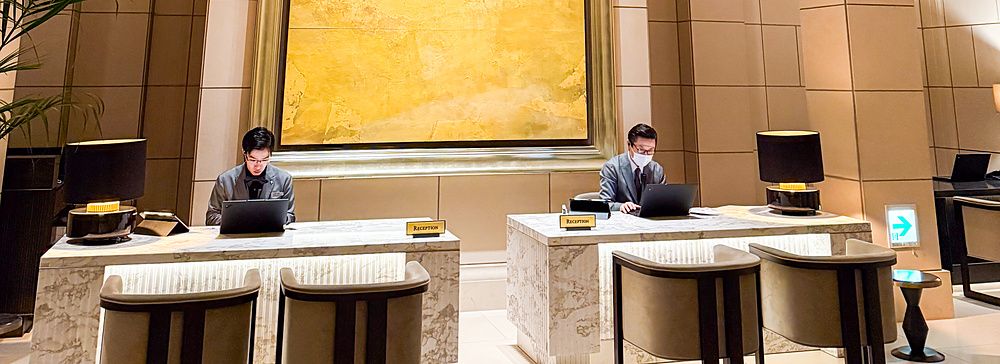 La reception a The St. Regis Osaka con due scrivanie in marmo, un grande dipinto dorato e un lampadario sferico.