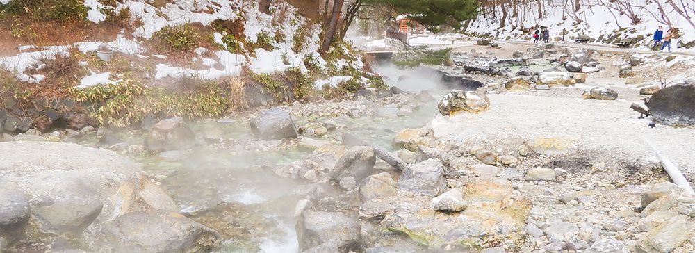 Veduta invernale di un ruscello termale nel Sainokawara Park, tra rocce, vapore e neve.