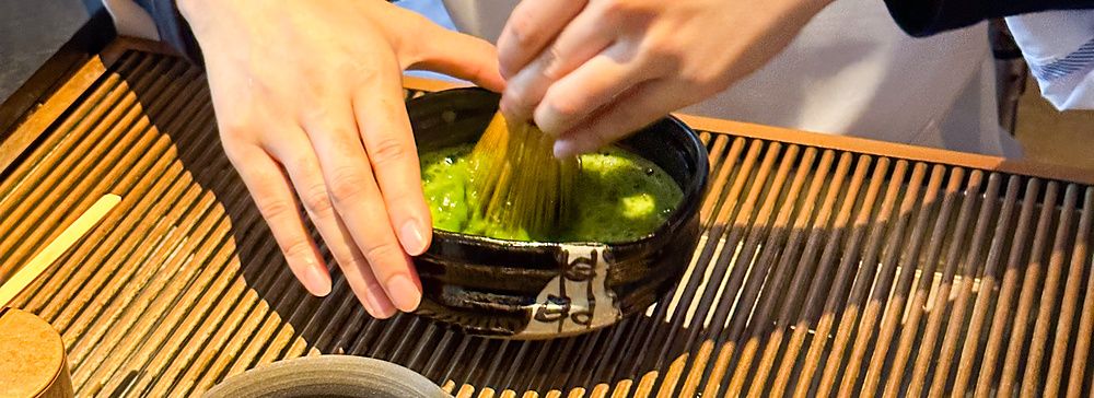 Preparazione del tè matcha a Sakurai Japanese Tea Experience con chasen su tavolo di legno.