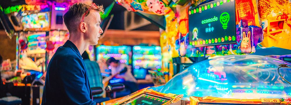 Persona gioca in una sala giochi giapponese, circondato da luci colorate.