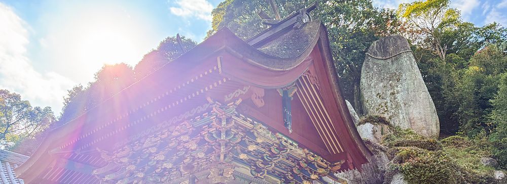 Veduta della struttura in legno rosso del Santuario Iwagami sull'isola di Awaji con il gigantesco masso sacro retrostante.