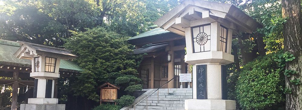 Due lanterne in pietra fiancheggiano il vialetto d'accesso verso una struttura in legno del Santuario Togo a Tokyo.
