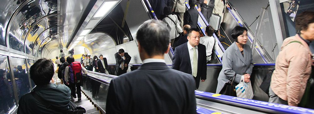 Molte persone si spostano sulle scale mobili all'interno di una moderna struttura tubolare di transito in Giappone.