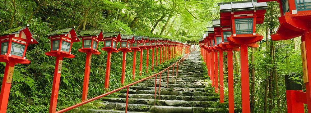 Scalinata in pietra che conduce al santuario di Kifune a Kyoto, fiancheggiata da caratteristiche lanterne rosse.