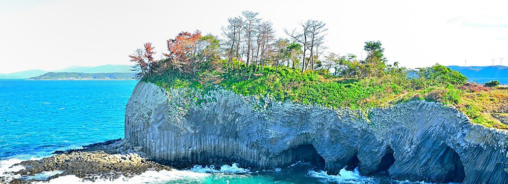Veduta panoramica delle scogliere di basalto di Nanatsugama a Karatsu con grotte marine e vegetazione sovrastante.