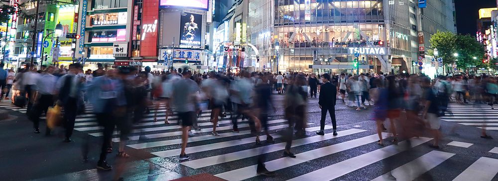 Veduta notturna dell'incrocio di Shibuya a Tokyo con una folla di persone in movimento che attraversano la strada.