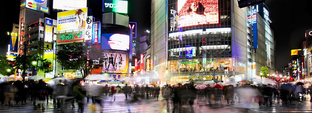 Incrocio di Shibuya a Tokyo con pioggia e persone sotto ombrelli.