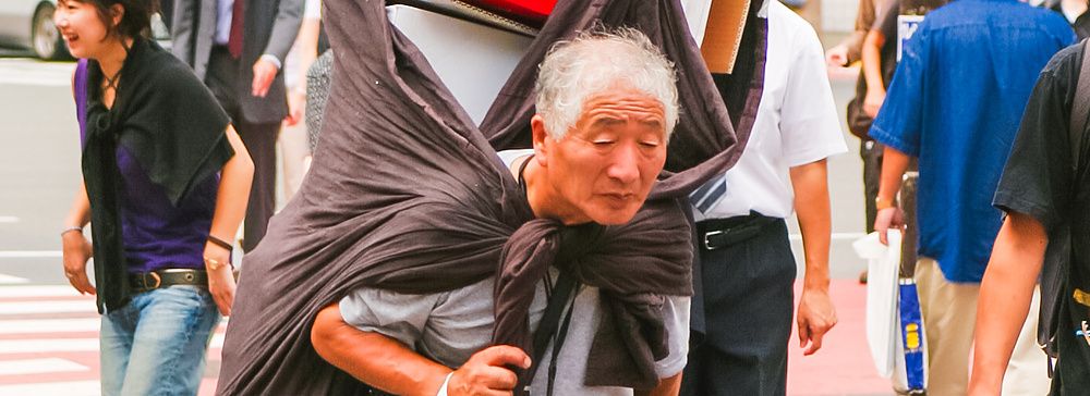 Un uomo anziano trasporta scatole sulle spalle per le strade di Shibuya.