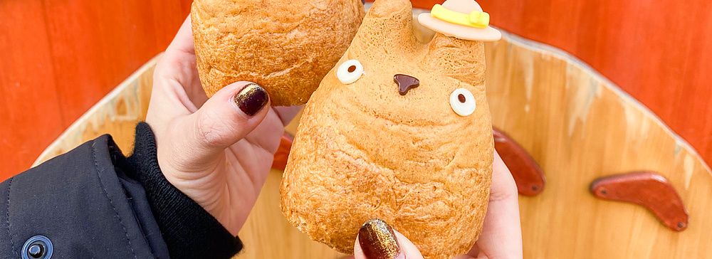 Due bignè a forma di Totoro tenuti in mano davanti a una decorazione in legno del personaggio presso la Shirohige’s Cream ...