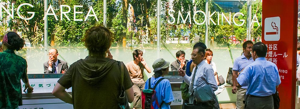 Gruppo di persone in una smoking area in Giappone, alcune fumano.