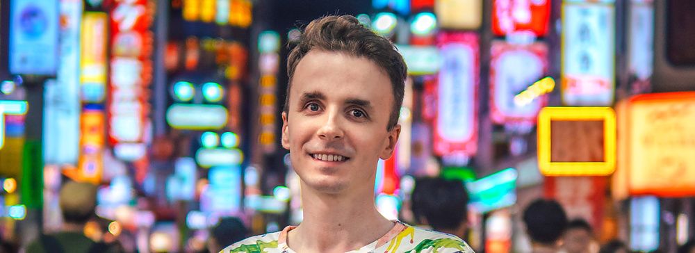 Marco Togni sorridente davanti alle luci vibranti di Shibuya di notte.