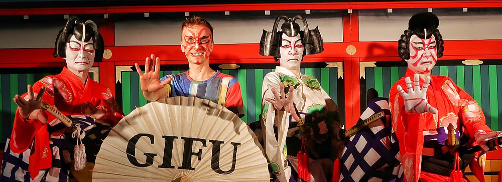 Persone in costumi tradizionali giapponesi posano con un grande ombrello a Gifu.