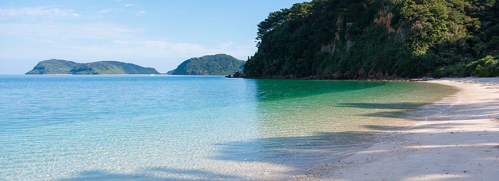 La spiaggia di Ida sull'isola di Iriomote presenta sabbia chiara e acque trasparenti vicino a un promontorio verde.