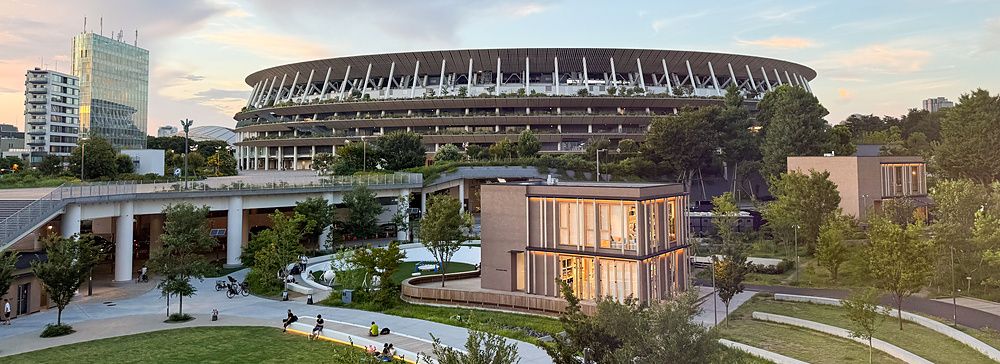 Lo Stadio nazionale del Giappone a Tokyo circondato dal verde di un parco urbano al tramonto.