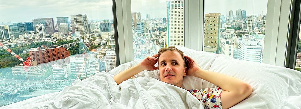 Marco Togni è a letto in una corner room dell'InterContinental the Strings Tokyo con vista panoramica sullo skyline urbano.
