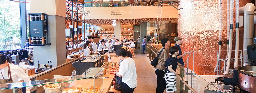 Interno dello Starbucks Reserve Roastery a Nakameguro con grandi tubi in rame, banconi e persone che visitano lo spazio.