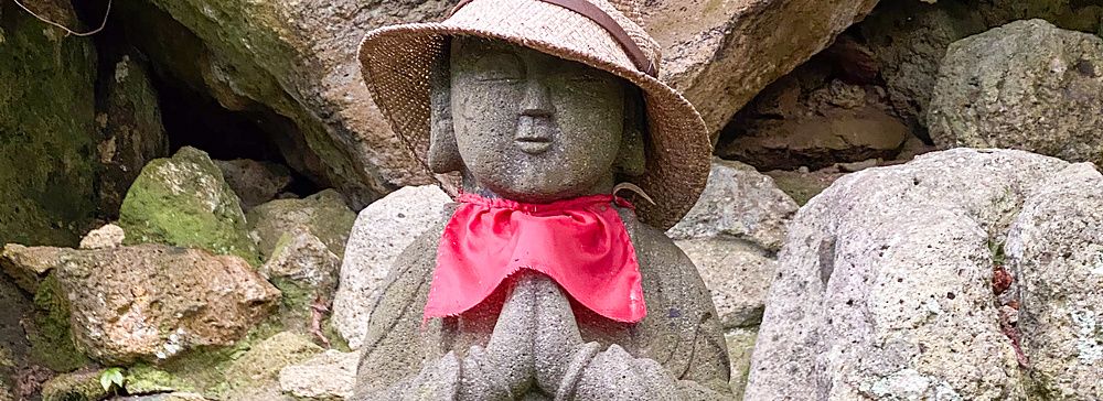 Statua di Jizo con cappello di paglia e bavaglio rosso tra le rocce.