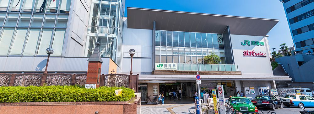 Ingresso della stazione ferroviaria JR Tabata a Tokyo con biciclette parcheggiate e cielo sereno.
