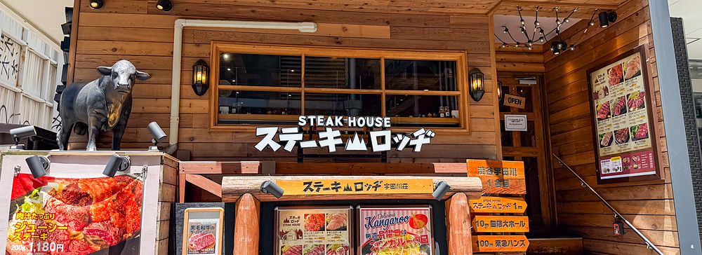 La facciata in legno del Ristorante Steak Lodge (Udagawacho), Shibuya, Tokyo, con insegne di menu e una statua di un toro.