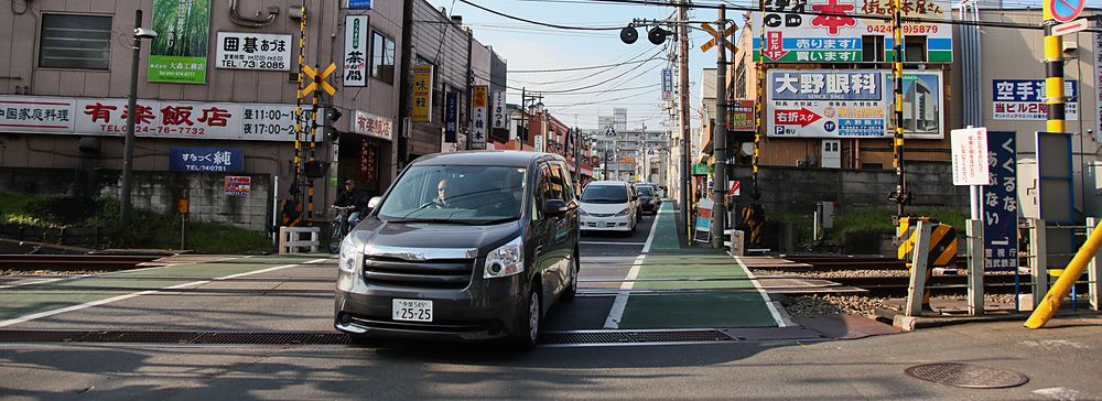 Auto che attraversano un passaggio a livello con edifici circostanti