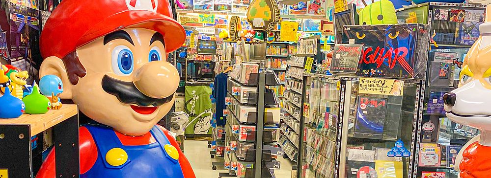 interno del negozio Super Potato ad Akihabara con videogiochi retrò e statua di personaggio videoludico.