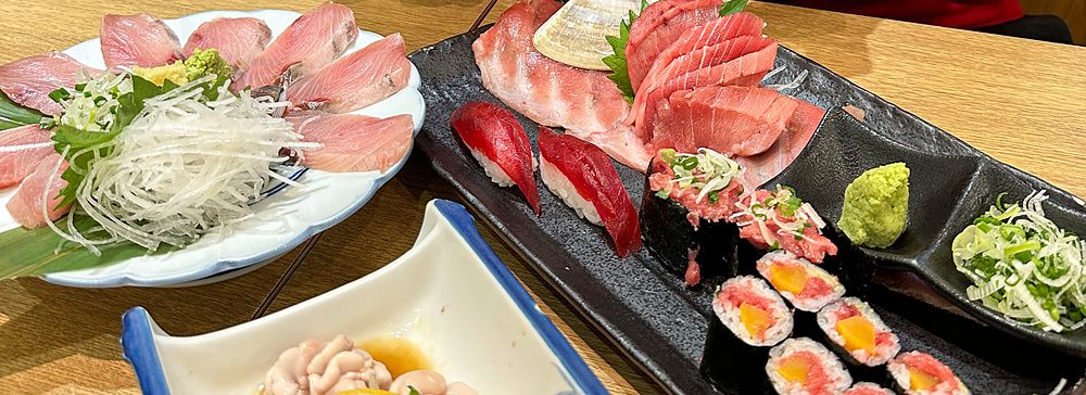 Marco Togni sorridente fa il gesto di vittoria davanti a piatti di sushi e sashimi nel ristorante Sushi no Darihan a Shinj...