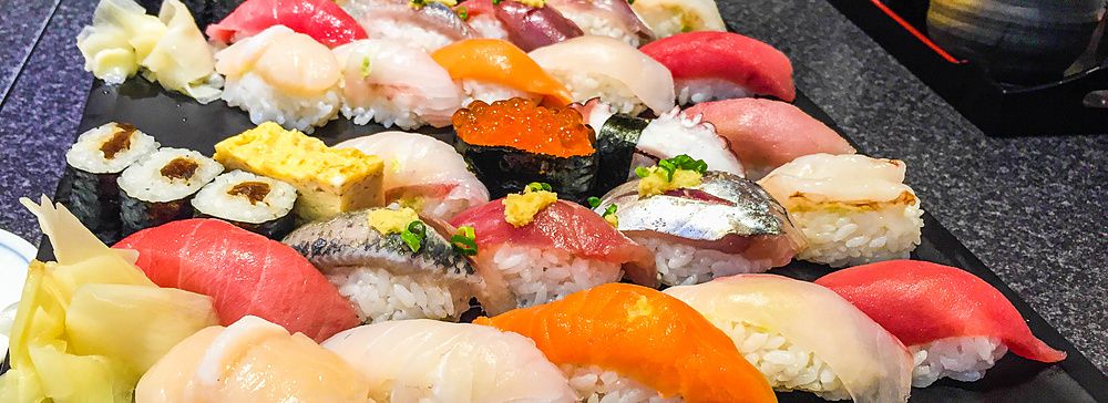 Piatto di sushi assortito su tavolo con persona in background.